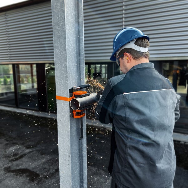 Handwerker mit Schutzhelm verwendet eine an einer Stütze befestigte Rohrschneidhilfe, um ein Metallrohr mit einem Winkelschleifer zu trennen.