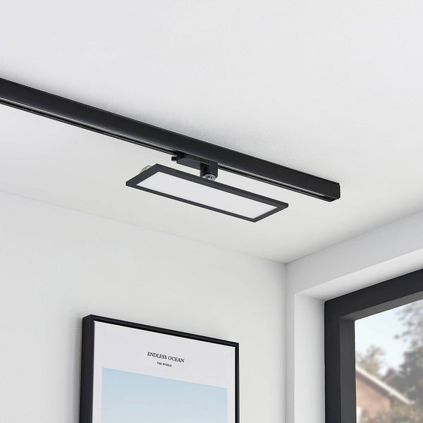 Modernes schwarzes LED-Schienensystem mit einer rechteckigen Panel-Leuchte an einer weißen Decke in einem hellen Raum.