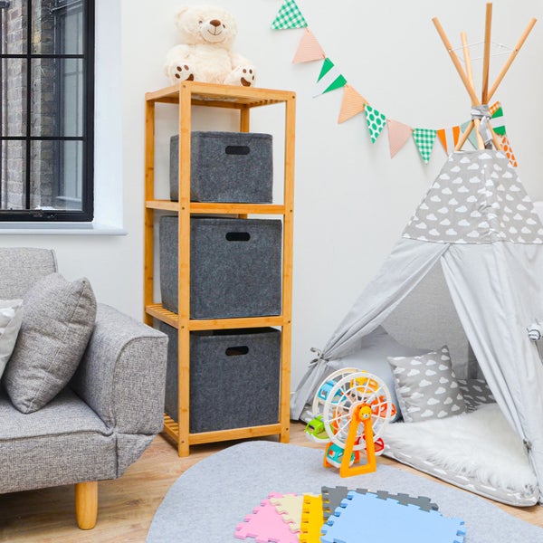 Ein Kinderzimmer mit einem Bambusregal, drei Filzboxen, einem Tipi Zelt, Spielzeug und einem Sofa in einer hellen und organisierten Umgebung.