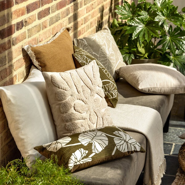 Dekorative Kissen auf einem Sofa vor einer Ziegelwand mit Pflanzen