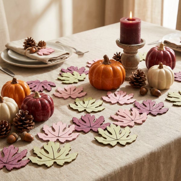 Herbstliche Tischdekoration mit Dekokürbissen, Tannenzapfen, Eicheln und ausgestanzten Holzblättern auf einer Leinentischdecke.