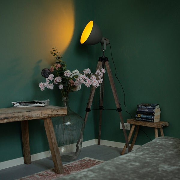 Moderne Stativstehleuchte mit Schirm und Holzdreibein in einem Raum mit rustikalen Holzhockern und einer Glasvase mit Blumen.