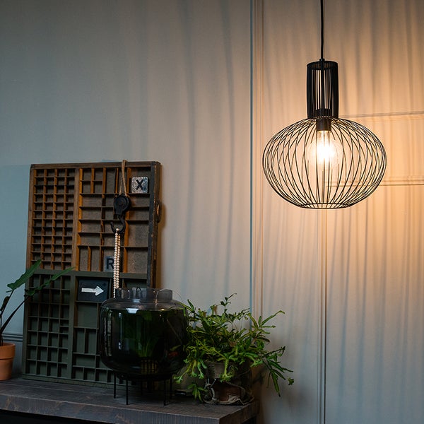 Dekorative Pendelleuchte aus Metall über einem Tisch mit Pflanzen und dekorativen Elementen