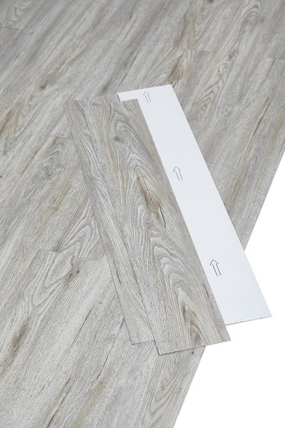 Selbstklebende Vinyl-Bodendielen in Holzoptik mit abziehbarer Schutzfolie und Richtungspfeilen.