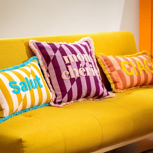 Gelbes Sofa mit dekorativen Kissen mit den Aufschriften Salut, Mon Chéri und Ciao