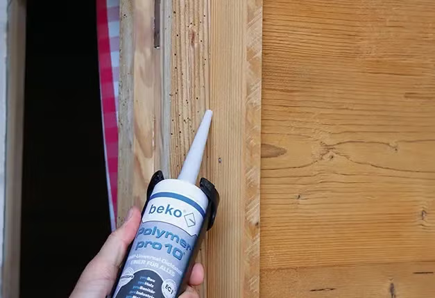 Hand hält eine Kartuschenpresse mit Beko Polymer Pro 10 Dichtstoff zum Auftragen auf eine Holztürzarge