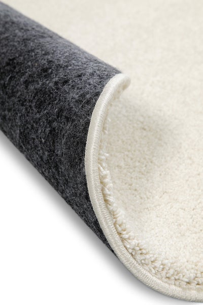 Detailansicht eines weichen, hellen Teppichs mit geketteltem Rand und dunkelgrauer Rückseite.