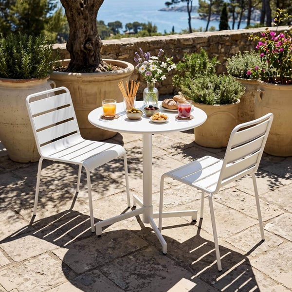 Sonnige Terrasse mit weißem Gartenmöbel-Set aus einem runden Tisch und zwei Metallstühlen, umgeben von großen Terrakotta-Pflanzgefäßen und Pflanzen.