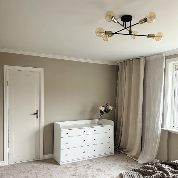 Schlafzimmer mit Deckenleuchte, Kommode und Vorhängen.