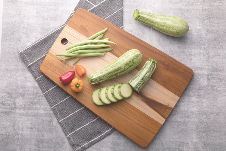 Holzschneidebrett mit Zucchini, grünen Bohnen und kleinen Paprikaschoten, Tramontina Logo auf dem Brett.