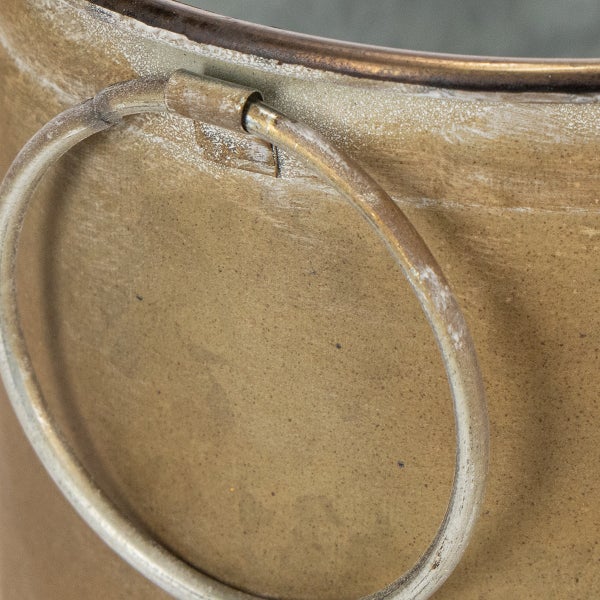 Detailansicht eines Übertopfs aus Metall mit einem seitlich angebrachten Ringgriff und antiker Oberfläche.