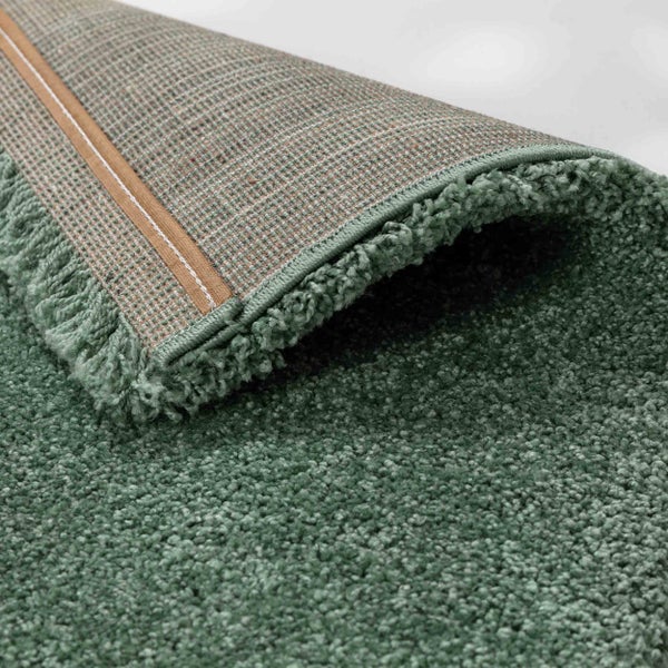 Grüner Hochflor-Teppich mit Textilrücken und eingefasster Kante.