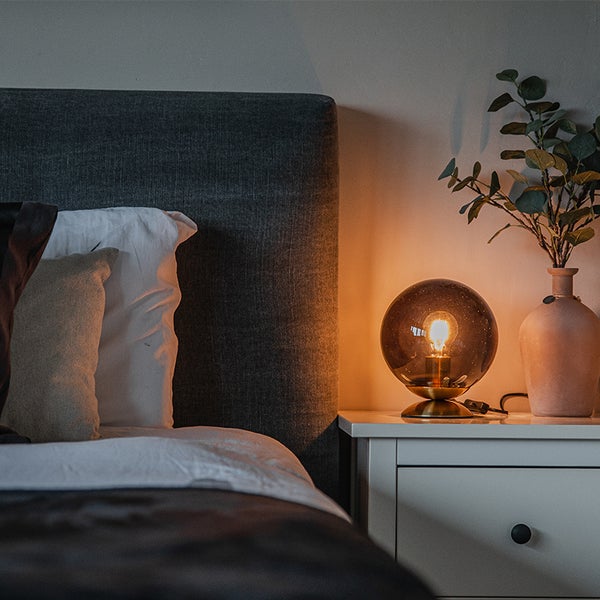 Nachttischlampe mit Glaskugel auf einem Nachttisch neben einem Bett.