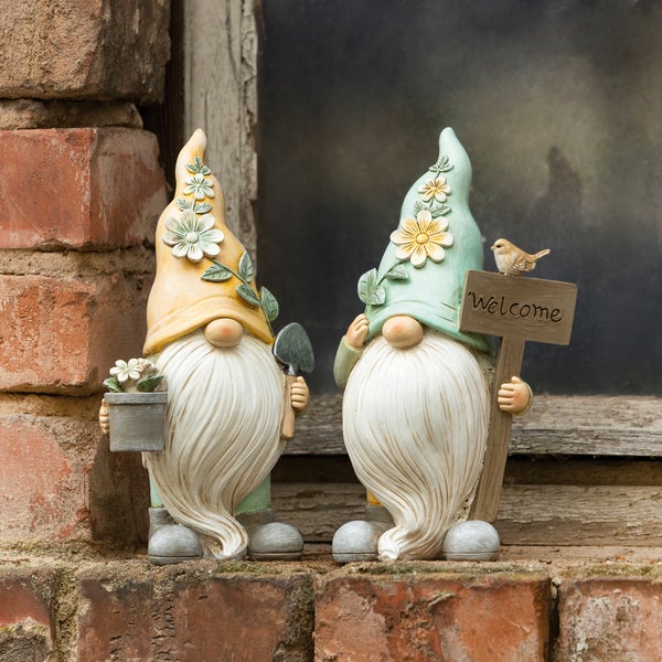 Zwei Gartenzwergfiguren mit Blumenhut, der eine mit einer Schaufel und einem Blumentopf, der andere mit einem Willkommensschild und einem Vogel