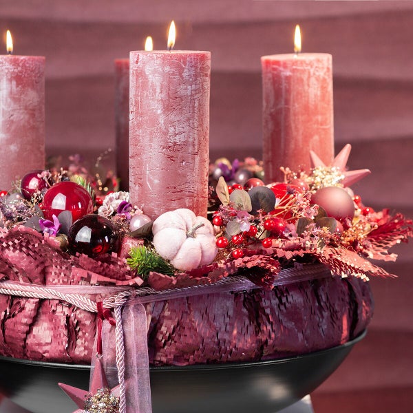 Festlicher Adventskranz mit vier Stumpenkerzen, dekoriert mit Weihnachtskugeln und kleinen Kürbissen in einer schwarzen Schale.
