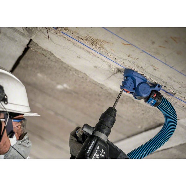 Ein Arbeiter bohrt mit einem Bohrhammer ein Loch in eine Betonwand. Eine Absaugvorrichtung ist am Bohrhammer befestigt.