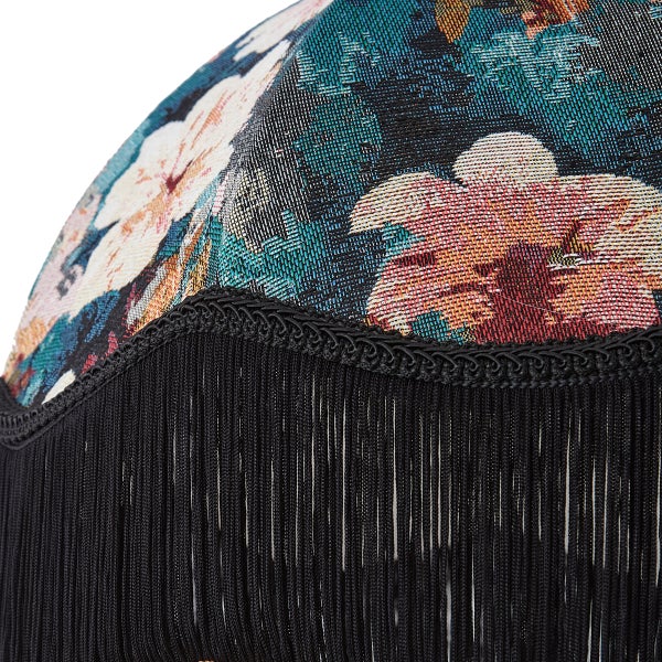 Detailansicht eines Lampenschirms mit gewebtem Blumenmuster und schwarzen Zierfransen.