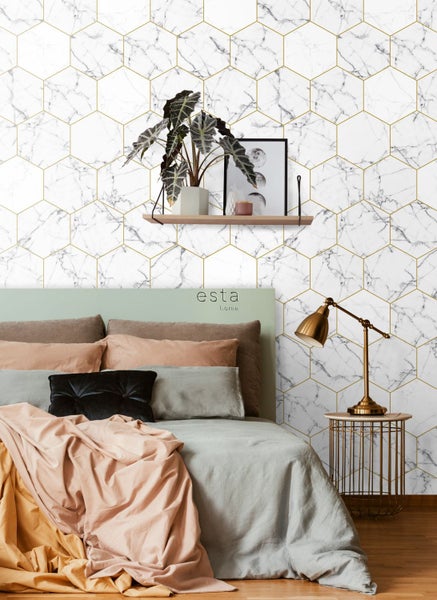 Schlafzimmer mit Bett vor einer weißen Tapete mit Marmoroptik und goldenem Hexagonmuster.
