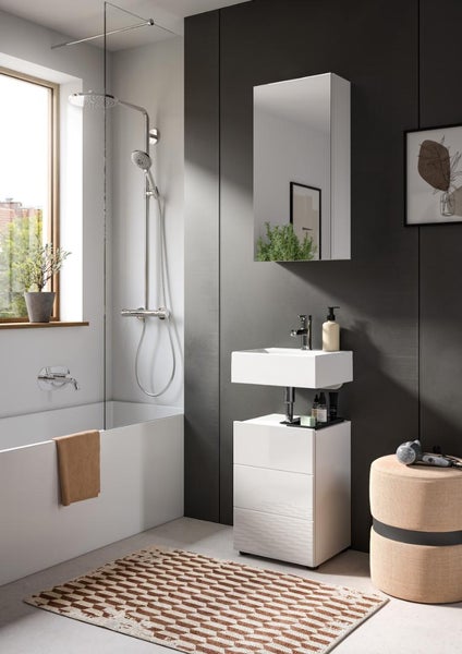 Modernes Badezimmer mit weißem Waschbecken, Unterschrank, Spiegelschrank, Badewanne mit Glaswand, Chromarmaturen und gemustertem Teppich.