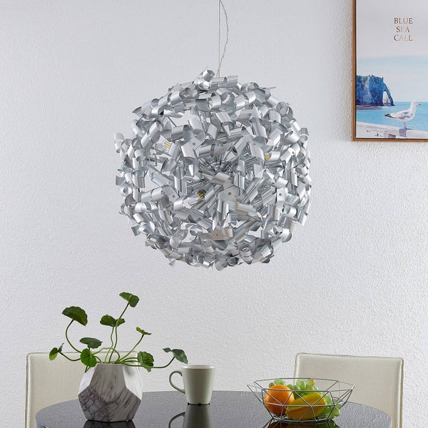 Silberne Pendelleuchte aus Metallstreifen über einem Esstisch mit Obstschale und Pflanze