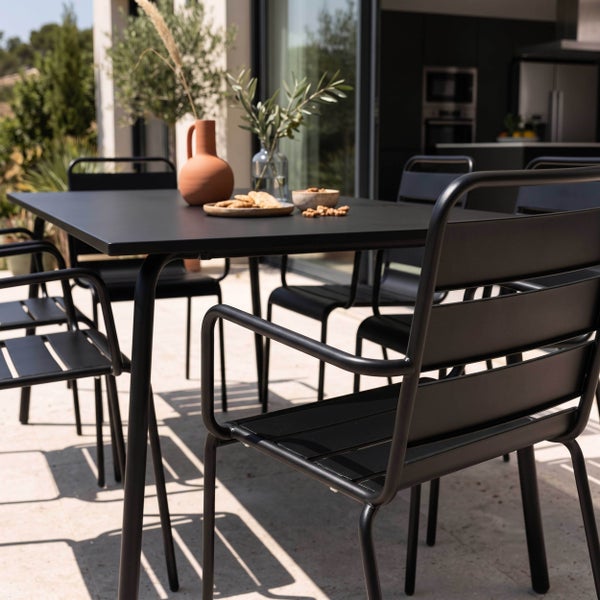 Modernes Gartenmöbel-Set bestehend aus einem schwarzen Metalltisch und passenden Stühlen auf einer hellen Steinterrasse.