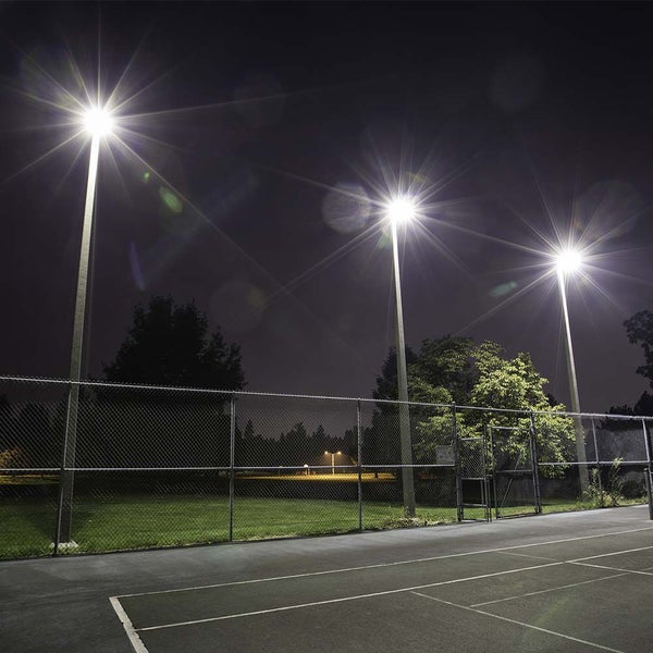 Beleuchteter Tennisplatz bei Nacht mit Zaun und Lampen