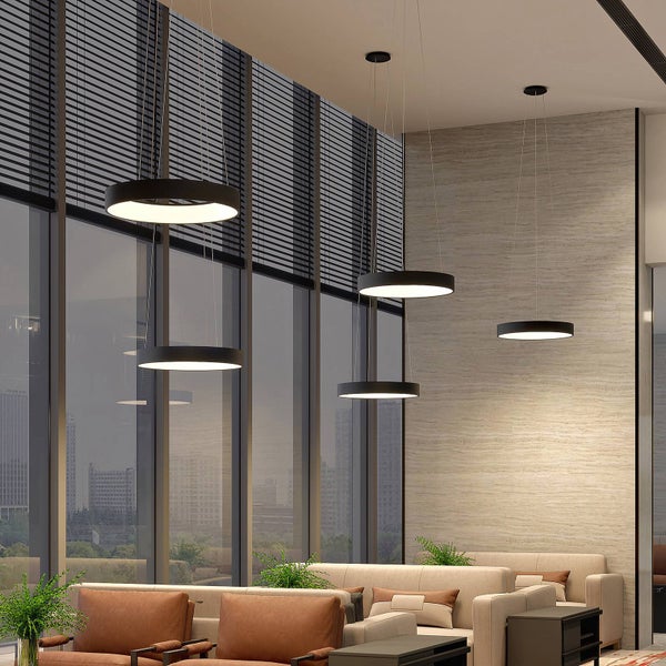 Moderne Lounge mit schwarzen ringförmigen Pendelleuchten in verschiedenen Höhen, großen Fenstern mit Stadtblick und beigen Sitzmöbeln.