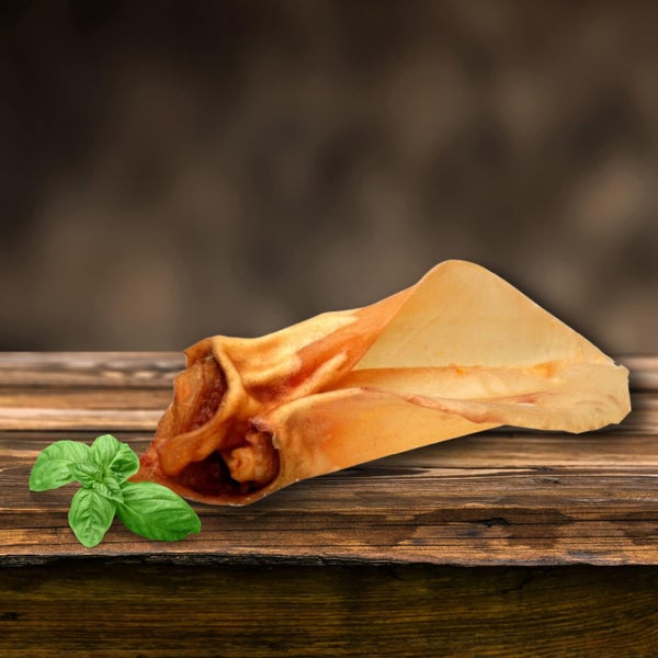 Schweineohr als Hundesnack auf einem Holztisch mit Basilikum