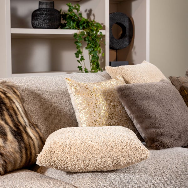 Dekorative Kissen in verschiedenen Texturen wie Bouclé, Kunstfell und mit Goldmuster auf einem hellen Sofa.