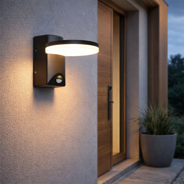 Moderne LED-Außenwandleuchte in Anthrazit mit Bewegungsmelder an einer Hauswand neben einer Holztür in der Abenddämmerung.