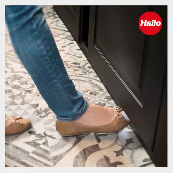 Hailo Logo. Eine Person öffnet einen Küchenschrank mit dem Fuß auf einem gemusterten Fliesenboden.