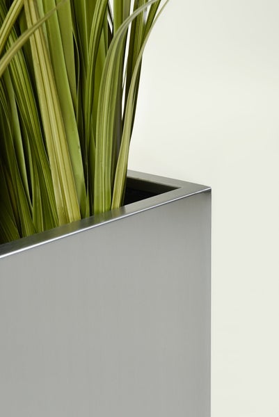 Detailansicht eines rechteckigen silbernen Metallpflanzgefäßes mit künstlichem grünem Gras.