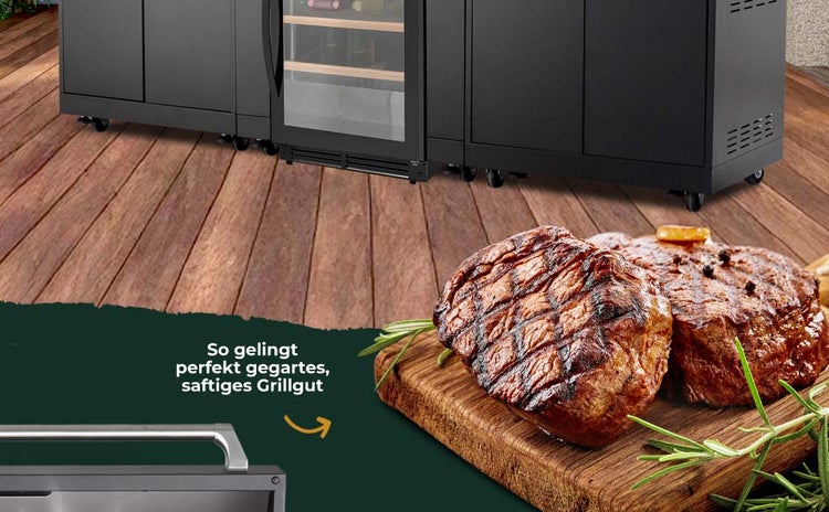 Modulare Außenküche auf einer Holzterrasse mit Schränken und Kühlschrank, im Vordergrund gegrillte Steaks auf einem Holzbrett.