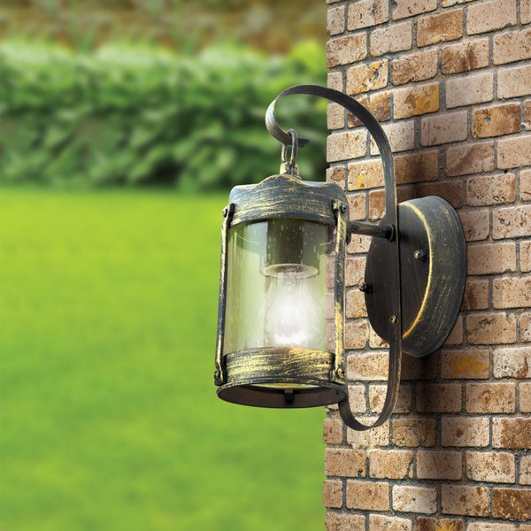 Antike Außenwandleuchte aus Metall und Glas an einer Ziegelwand mit Garten im Hintergrund.