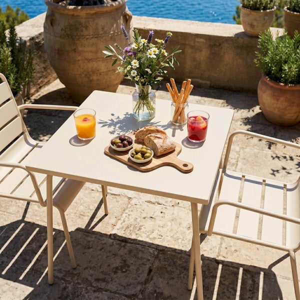 Helle und organisierte Gartensitzgruppe aus einem quadratischen Metalltisch und zwei Gartenstühlen auf einer Terrasse.