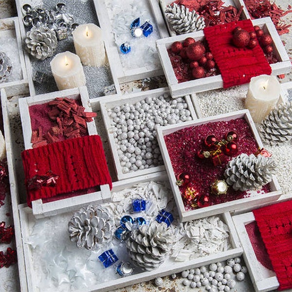Weihnachtsdekoration in Holzfächern mit Zapfen, Kerzen, Christbaumkugeln und Granulat in Rot und Weiß.