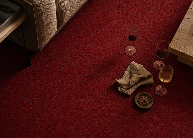 Roter strukturierter Teppichboden in einem Wohnzimmer mit Weingläsern, einer beigen Serviette und Snacks neben einem Sofa.