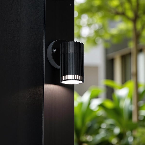 Eine zylindrische Wandleuchte aus Metall ist an einer Säule montiert.