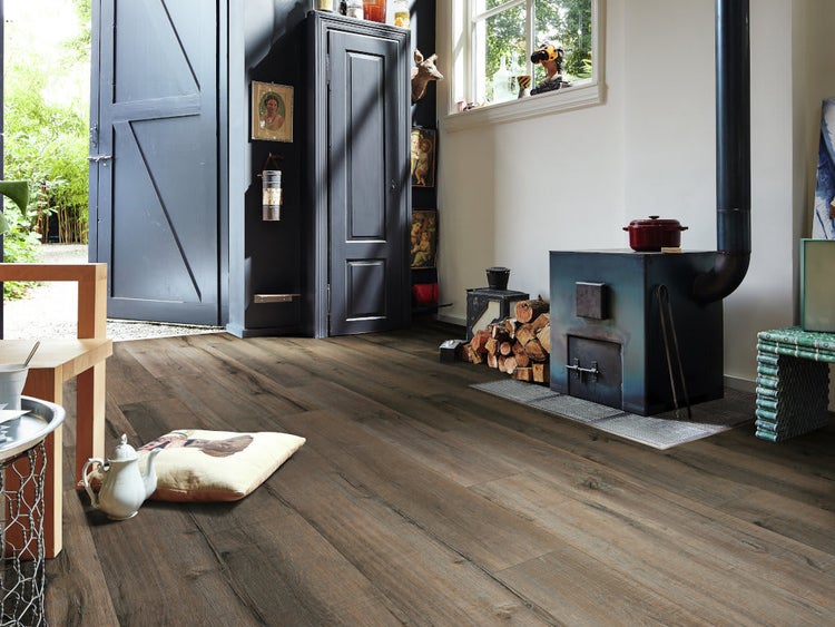 Wohnraum mit rustikalem Laminatboden in Holzoptik, offener Tür zum Garten, Kaminofen und gemütlicher Einrichtung.