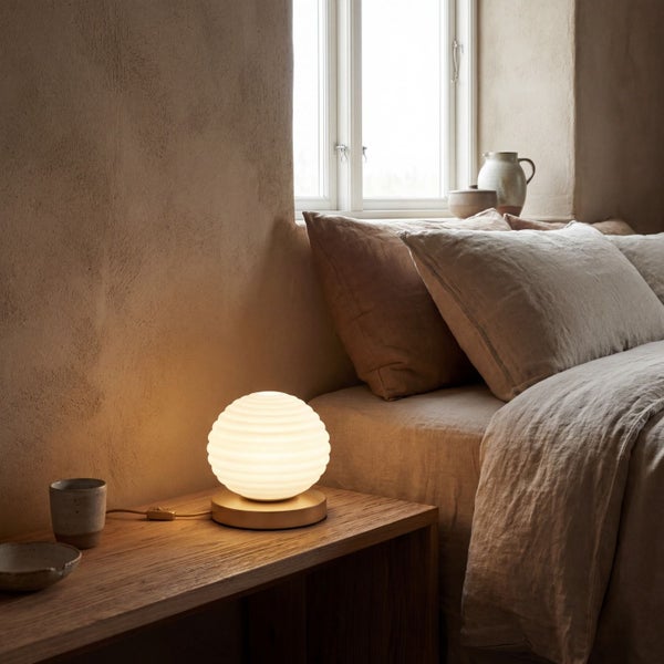 Moderne kugelförmige Tischleuchte mit gerippter Oberfläche auf einem Nachttisch aus Holz neben einem Bett im Schlafzimmer.