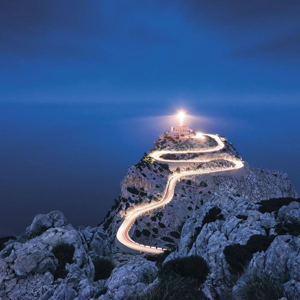 Beleuchteter Leuchtturm auf einem Berg mit gewundener Straße.