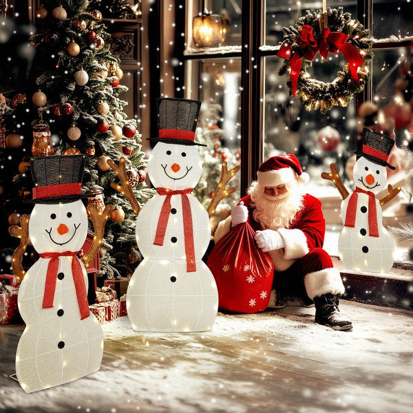 Weihnachtliche Szene mit drei unterschiedlich großen, beleuchteten LED-Schneemännern mit Zylindern und Schals neben einem Tannenbaum.