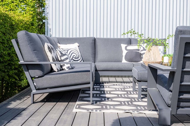 Modernes L-förmiges Garten-Lounge-Set mit dunkelgrauen Polstern und Metallgestell auf einer Holzterrasse mit geometrischem Teppich.