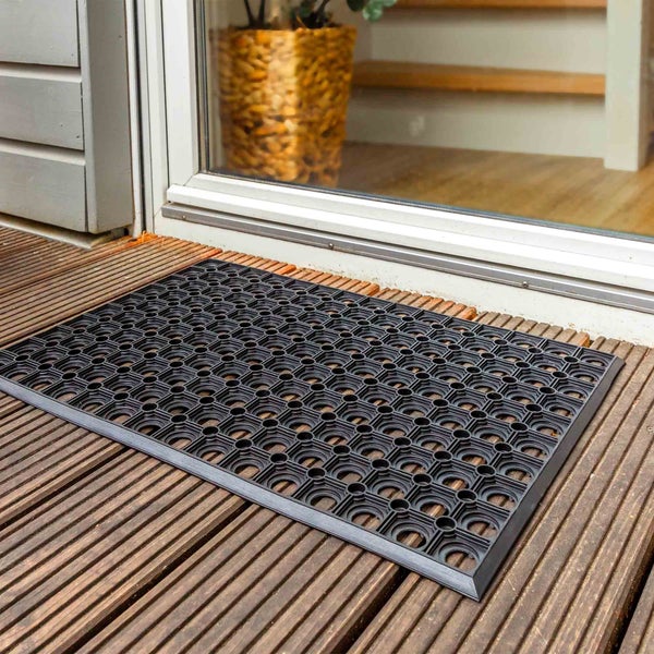 Schwarze Fußmatte aus Gummi vor einer Haustür auf einem Holzdeck