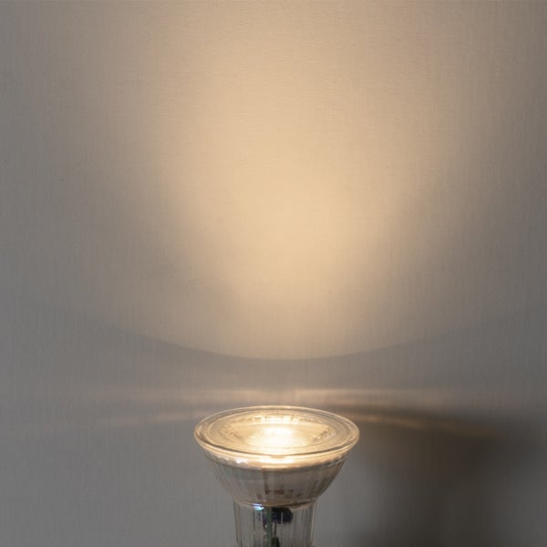 Eingeschaltete Reflektorlampe mit warmweißem Lichtkegel an einer Wand.