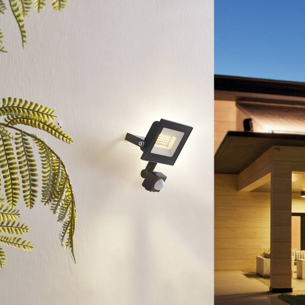 LED-Außenstrahler mit Bewegungsmelder an einer Hauswand montiert, der den Bereich eines modernen Gebäudes beleuchtet.