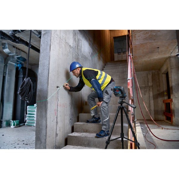 Handwerker arbeitet mit einem Linienlaser auf einer Baustelle. Der Laser steht auf einem Stativ.