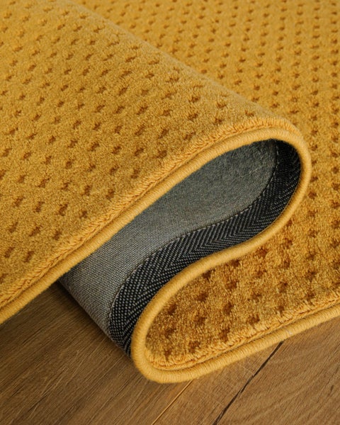 Gelber Teppich mit strukturierter Oberfläche und rutschfester Rückseite auf einem Holzboden.