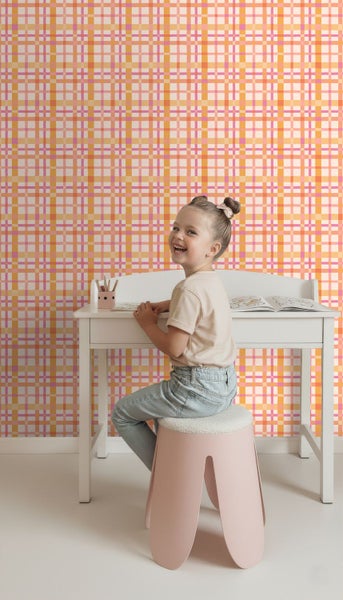 Karierte Tapete in Orange, Rosa und Gelb in einem hellen Kinderzimmer hinter einem weißen Schreibtisch.