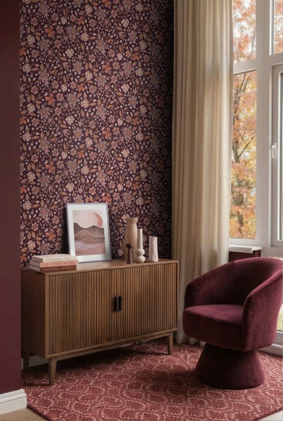 Vliestapete mit Blumenmuster in einem gemütlich eingerichteten Wohnraum mit Holzkommode und Sessel.